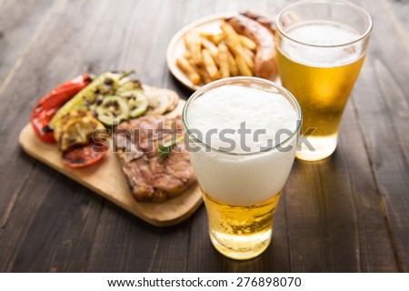 Beer in glass with gourmet steak and french fries on wooden background