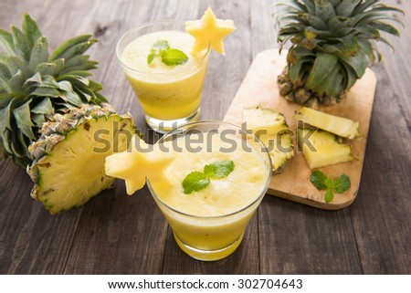 Pineapple smoothie with fresh pineapple on wooden table.