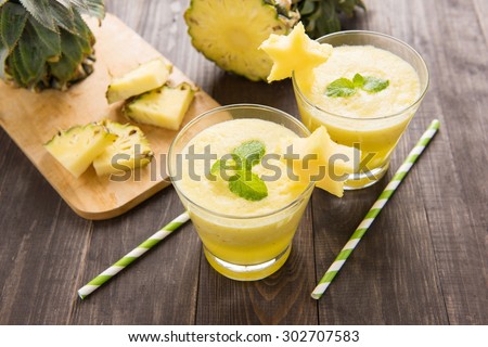Pineapple smoothie with fresh pineapple on wooden table.