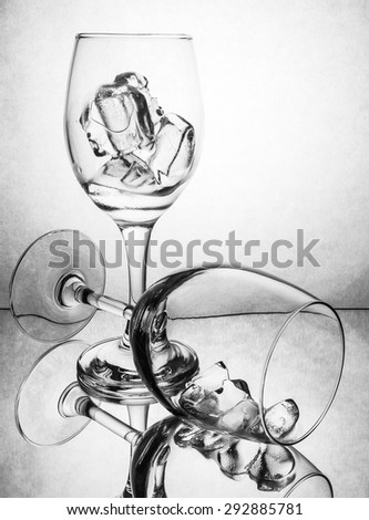 Black and white of wine glass with ice reflected on mirror and white paper background