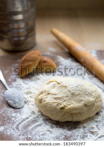 Wooden rolling pin with can of flour, dough and pastry on a wooden table