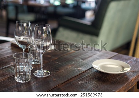 Glasses, flowers, forks, knives served for dinner in restaurant with cozy interior.