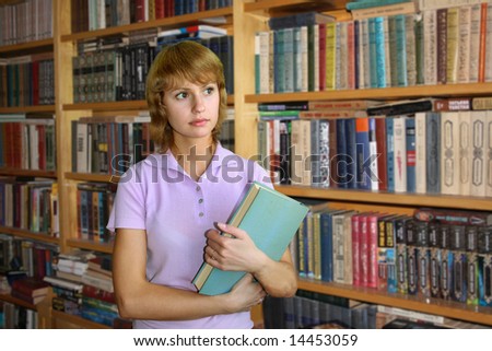The girl in a pink shirt with the big book on a background of book racks.