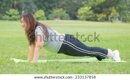 Obese women do push ups on the grass.