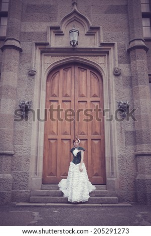 A woman like a princess in an vintage dress beside old castle. Mysterious woman dressed in scenic fashion clothes.