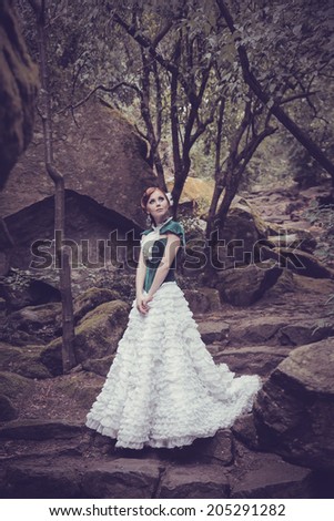 A woman like a princess in an vintage dress in fairy park. Mysterious woman dressed in scenic fashion clothes. Green labyrinth.