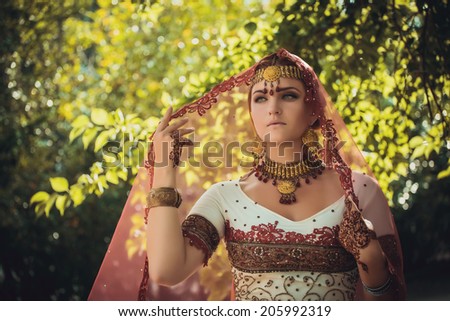 Beautiful young indian woman in traditional clothing with bridal makeup and jewelry. gorgeous brunette bride traditionally dressed Outdoors in India. Girl bollywood dancer in Sari and henna on hands