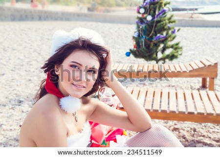 Resting woman on winter vacation in warm places. Happy Santa Girl with sunglasses on tropical beach. Beautiful brunette young woman smiling portrait in red Christmas hat celebrating New Year.