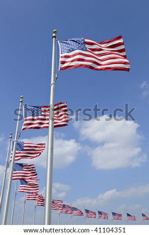 Many American flags blowing in the breeze against blue sky