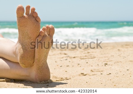 Close up of sandy feet relaxing on a beautiful beach, with waves breaking in the background.