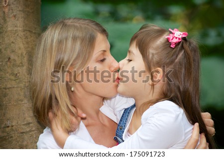 mother and daughter hug and kiss in park