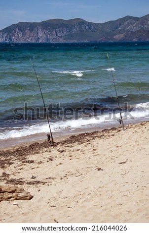 two fishing rods in the sea on the sand with mountains on the background