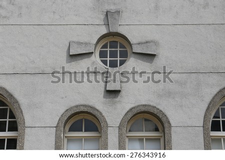 A round window with rectangular stone ornament around it. Looks like a cross.