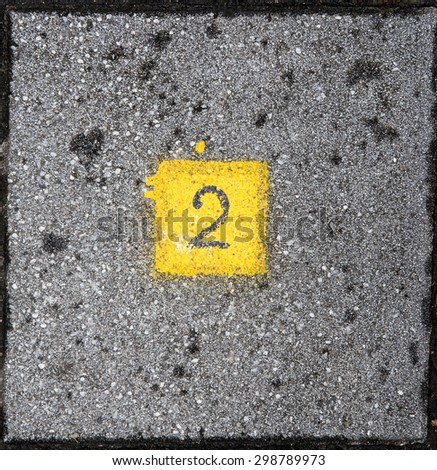 Number two written in a yellow square on grey brick ground.