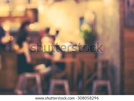 De focused/Blur image of a girl standing and a boy sitting in front of a open cafe. Blurred people in cafe. Vintage effect.