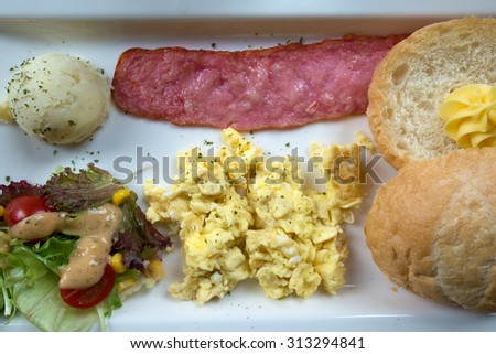 Breakfast consists of a slice of ham, bread, salad, potato salad ball and scrambled eggs on a white plate. Retro effect. Toned image.
