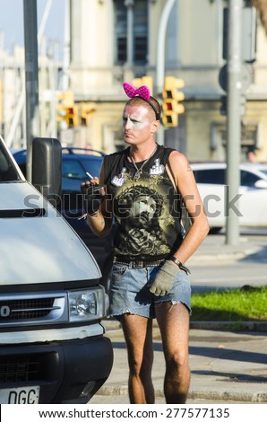 BARCELONA, SPAIN - OCTOBER 6, 2014: A man waering a fancy dress and a pink bow on his head smokes a cigarette on a city street.