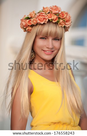 Beautiful young woman with flowers wreath and bouquet lifestyle portrait, happy blonde girl walking on street at summer vacation. Happy woman face outdoors.