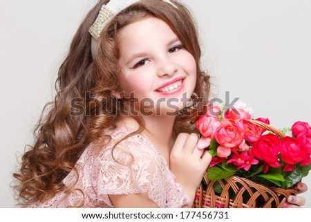 Cute little child girl with spring flowers, happy baby girl with basket of flowers. Isolated in studio on white background.