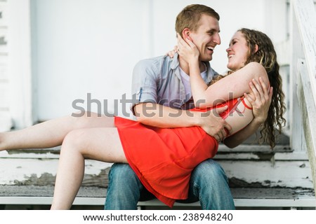 Young Attractive Couple Woman in red dress on lap laughing with each other sitting down on steps