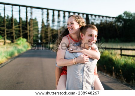 Woman on Back of Attractive Male Walking On Country Roads Smiling Off Camera