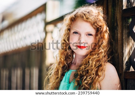 attractive young red head leaning against fence looking at camera slight smile