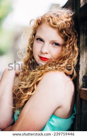 attractive young red head leaning against fence looking at camera slight smile, hugging herself, variation