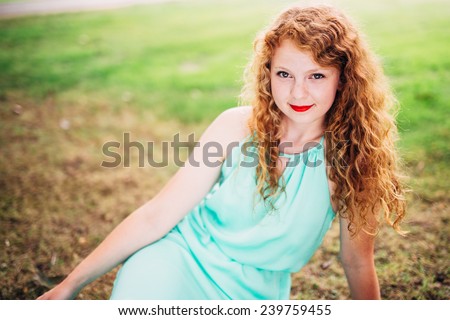 attractive young red head sitting in grass slight smile