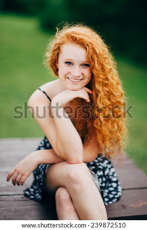 Attractive Young Female Redhead, smiling, hand under chin, sitting on table