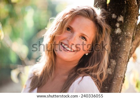 Beautiful Blonde Young Woman leaning on tree zoom vertical big smile