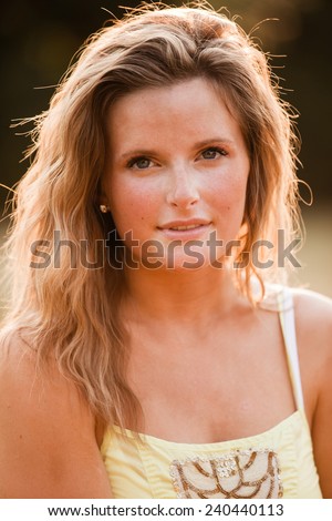 Beautiful Blonde Young Woman in sunset meadow summer day hand on arm no smile vertical