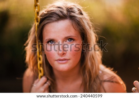 Beautiful Blonde Young Woman smiling on swing no smile head against chain close up