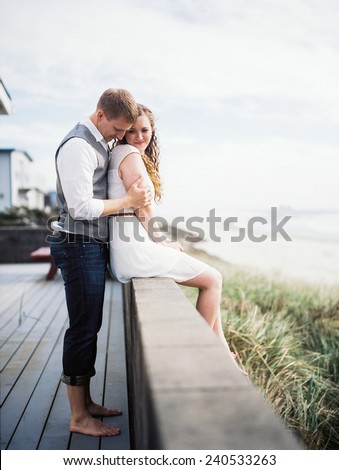 Attractive Young Blond Couple, woman sitting on ledge on beach, man standing behind her