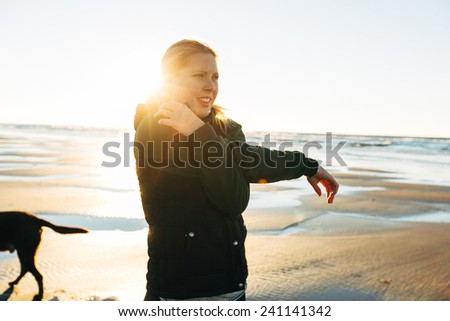 Female Runner on the Beach at Sunset stretching arm with sun behind