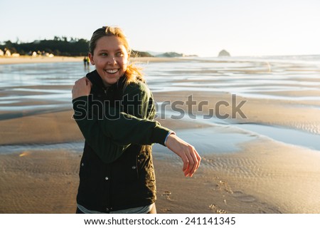 Female Runner on the Beach at Sunset stretching arm laughing away from camera