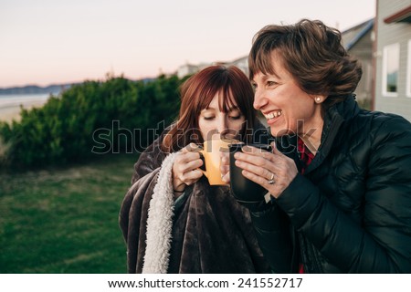 Mother and Daughter Drinking from Coffee Cups at Sunset at the Beach laughing