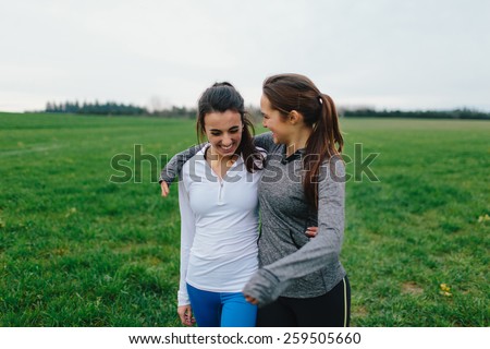 Young Adult Female Runners Arms Around each other smiling in country field
