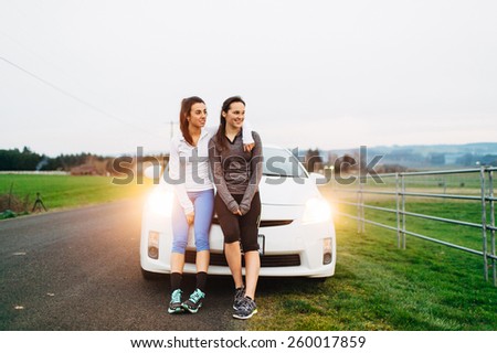 Young Adult Females resting on car after run with lights on