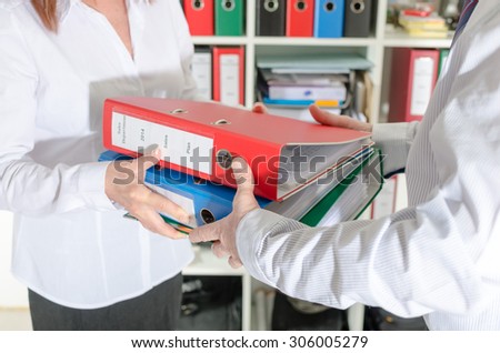 Secretary giving binders to her manager at office