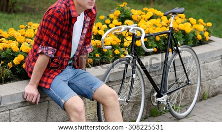 Hipster man with bicycle resting over flowerbed withal yellow flowers. WIthout face. Side view
