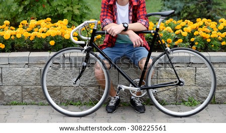 Hipster man with bicycle resting over flowerbed withal yellow flowers. Without face. Front view