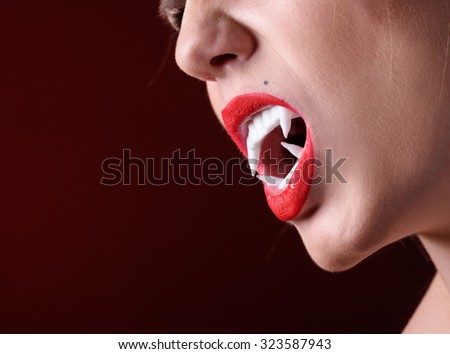 Close up shot of woman vamire mouth with white fangs.