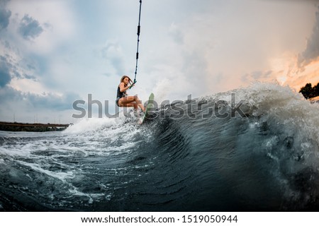 Young sporty girl rides on a green and orange wakeboard in the river near forest Stock fotó © 