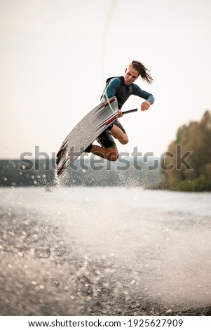 young adult guy in wetsuit and vest jumps spectacularly on wakeboard above the water with splashes Stock fotó © 