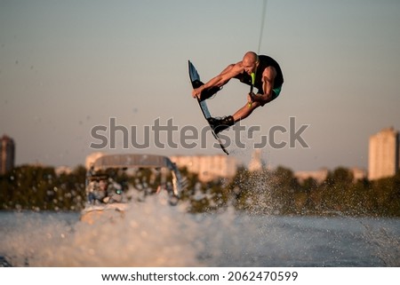 energy muscular male wakeboarder makes extreme stunts jumping on wakeboard over splashing wave. Wakeboarding and water sports activity. Stock fotó © 