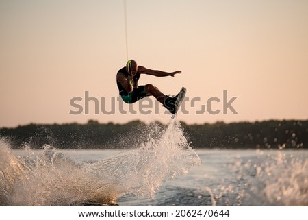 healthy strong muscular man holding rope and jumping with wakeboard over splashing water. Summertime watersports activity Stock fotó © 