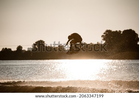 beautiful view of active male wakeboarder making extreme stunts jumping and flips on wakeboard over water. Summertime watersports activity Stock fotó © 