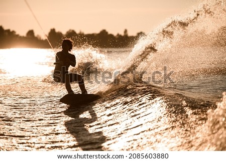 Great view of silhouette of female rider holding rope and rides down on wakeboard on splashing wave. Water sports activity. Stock fotó © 