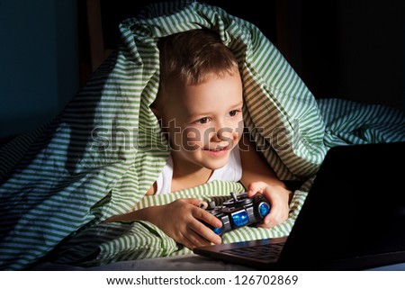 five years old happy kid hiding under blanket playing computer games