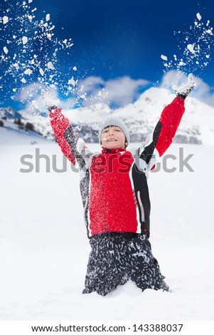 Happy smiling boy throws snow in the air with snowflakes flying in all directions